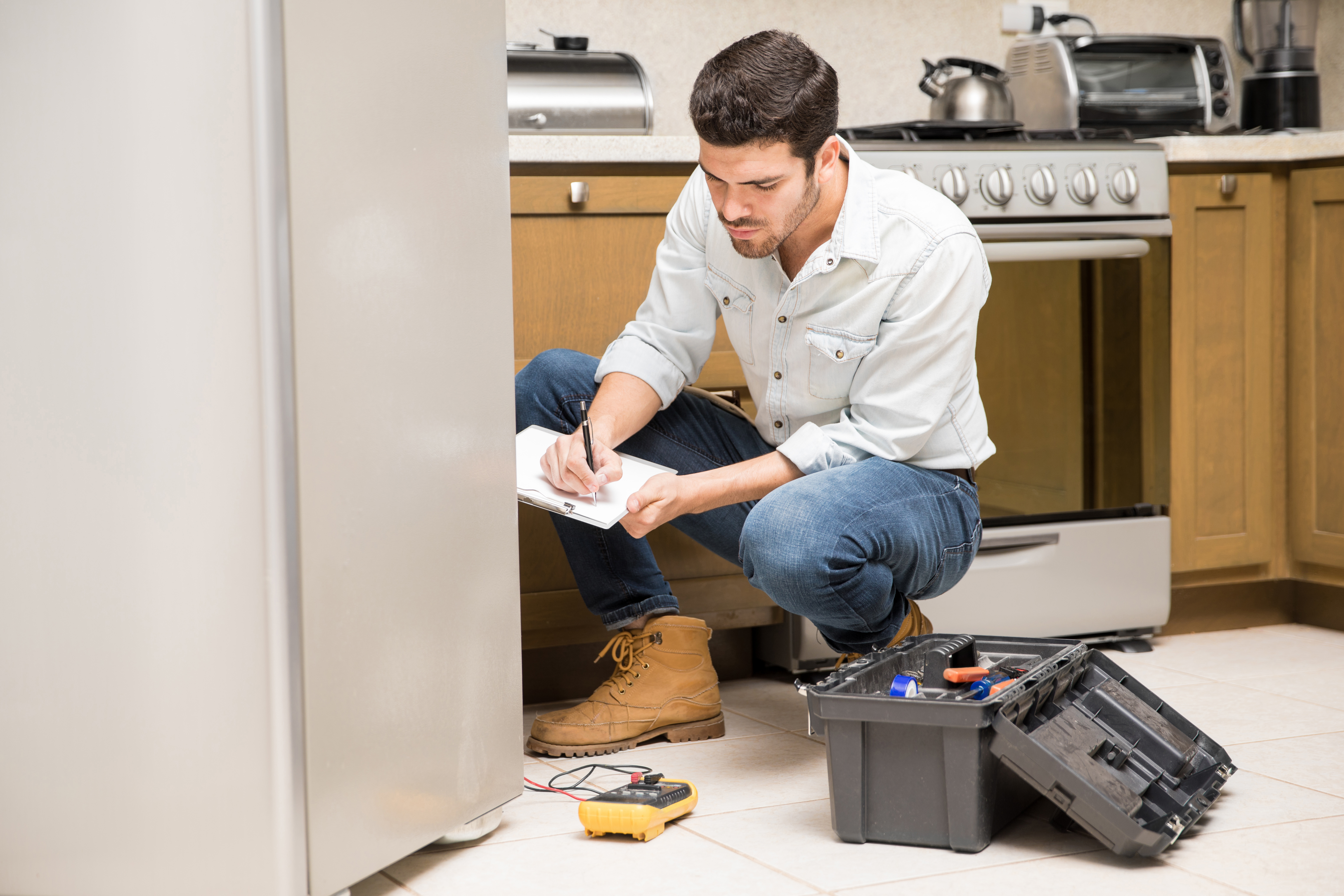 HVAC technician inspecting and documenting refrigerator repair findings in a home kitchen